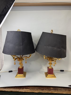 Lot 790 - A PAIR OF GILT METAL TABLE LAMPS ON RED STONE BASES WITH BLACK SHADES