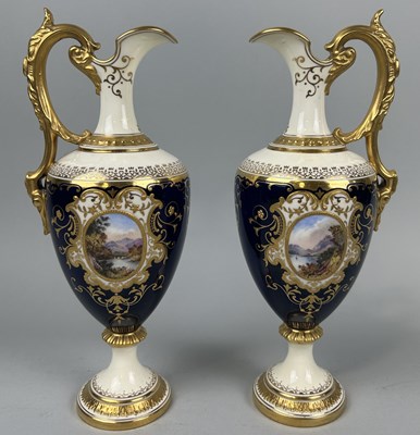 Lot 667 - A PAIR OF COALPORT PORCELAIN EWERS BLUE GROUND WITH GILT AND CENTRAL PAINTED PANELS DEPICTING LANDSCAPE SCENES